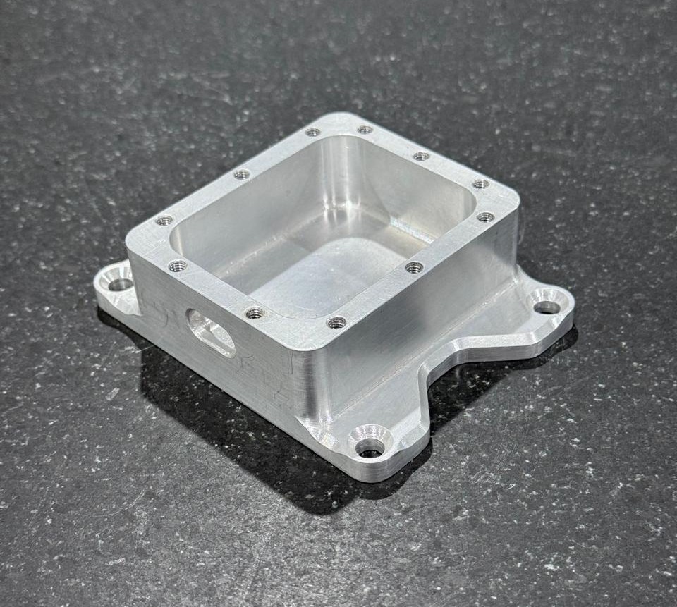 A CNC machined Aluminum 6061 housing part demonstrating non-optimized design features, including perfectly sharp internal corners and excessively deep blind threaded holes.