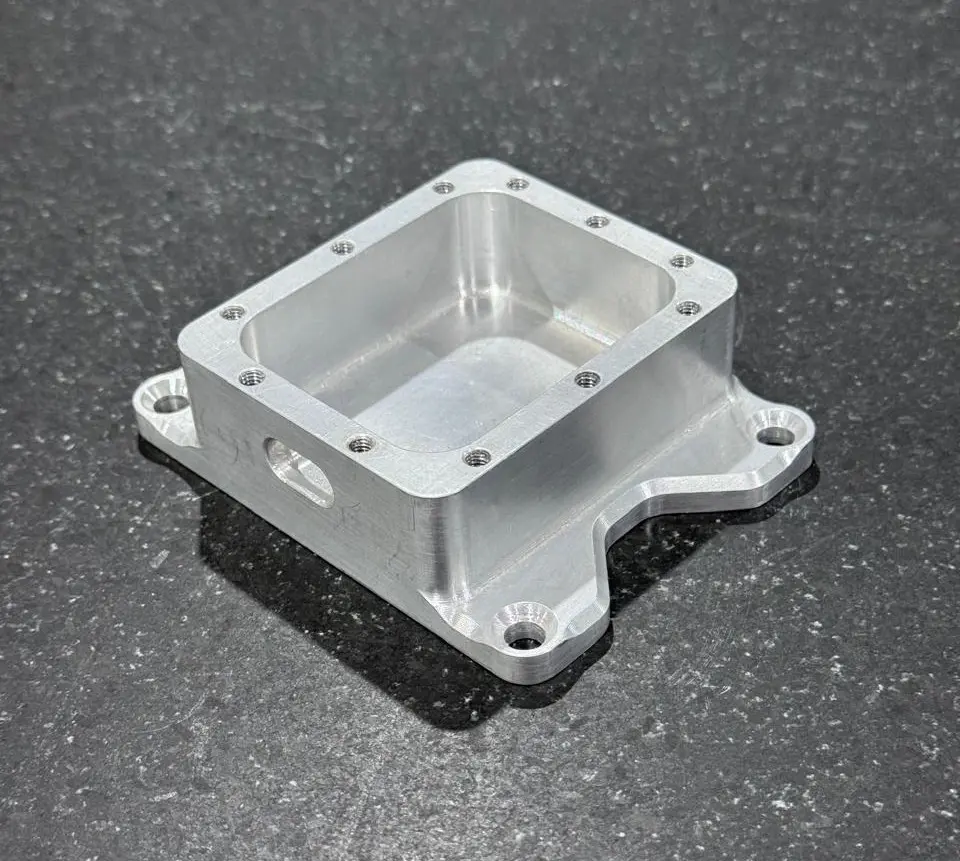 A CNC machined Aluminum 6061 housing part demonstrating non-optimized design features, including perfectly sharp internal corners and excessively deep blind threaded holes.